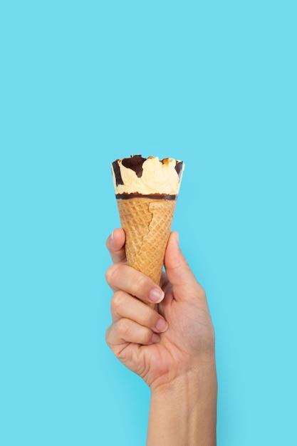 Mão segurando a casquinha de sorvete no fundo azul