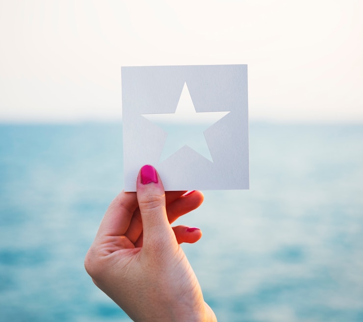 Foto grátis mão segurando a forma de estrela de papel perfurado com fundo de oceano