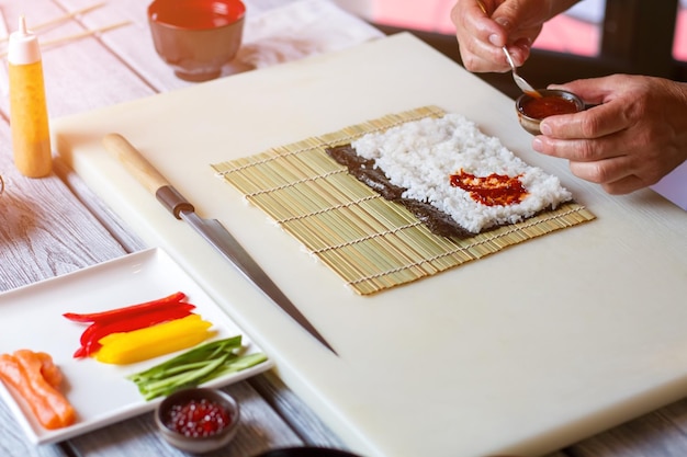 Mão segurando a tigela com molho. molho vermelho com arroz branco. tempero para rolos de futomaki. receita original do chef do restaurante.