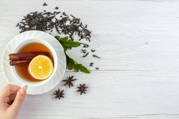 Mão segurando chá preto em uma xícara branca em torno de chá seco e folhas
