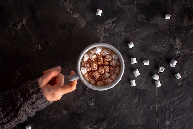 Mão segurando chocolate quente com marshmallows e cacau em pó