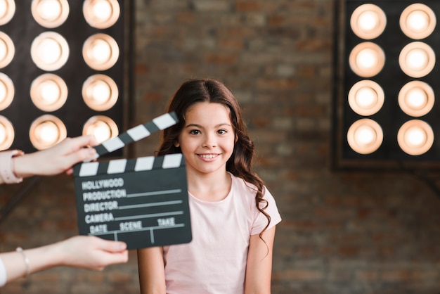 Foto grátis mão segurando claquete na frente da menina sorridente