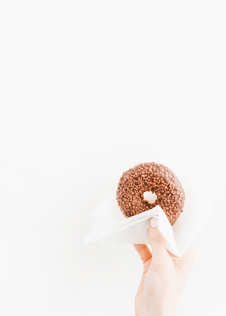 Mão segurando donut de chocolate com papel de seda no fundo branco