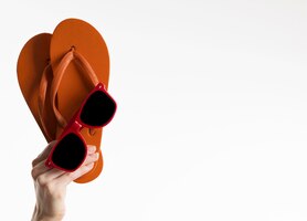 Foto grátis mão segurando flip-flops com óculos de sol e espaço de cópia
