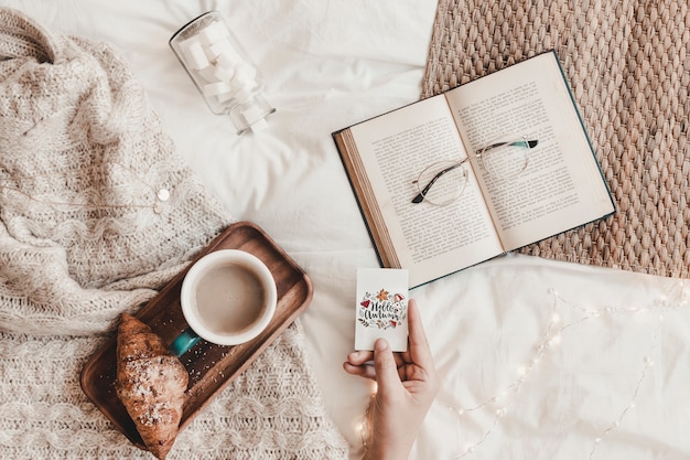 Mão segurando fraque perto de livro, óculos, comida e manta