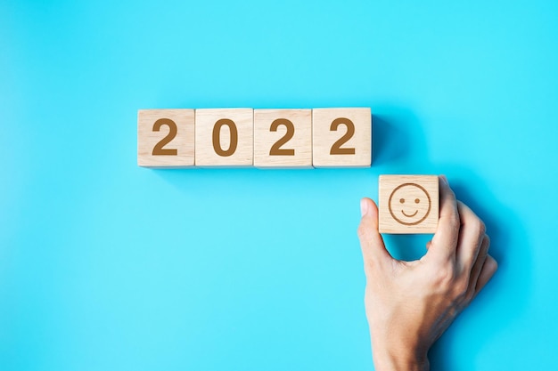 Mão segurando o bloco de rosto de sorriso com 2022 texto sobre fundo azul. conceitos de satisfação, feedback, revisão e ano novo