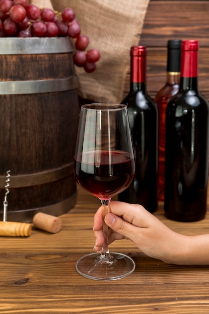 Mão segurando o copo de vinho com garrafas e barre