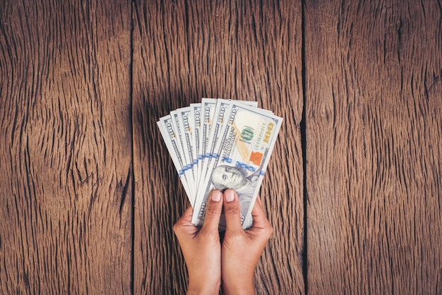 Foto grátis mão segurando o dinheiro de notas de dólar em fundo de madeira