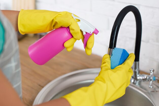 Mão segurando o frasco de spray e esponja durante a limpeza da pia em casa