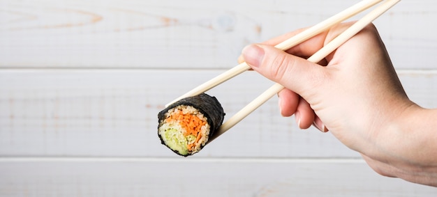 Mão segurando os pauzinhos e rolo de sushi
