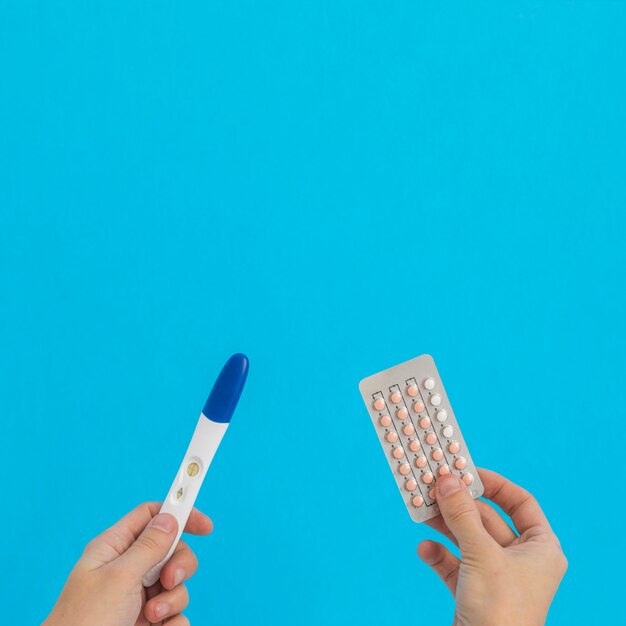 Mão segurando pílulas anticoncepcionais ee teste de gravidez