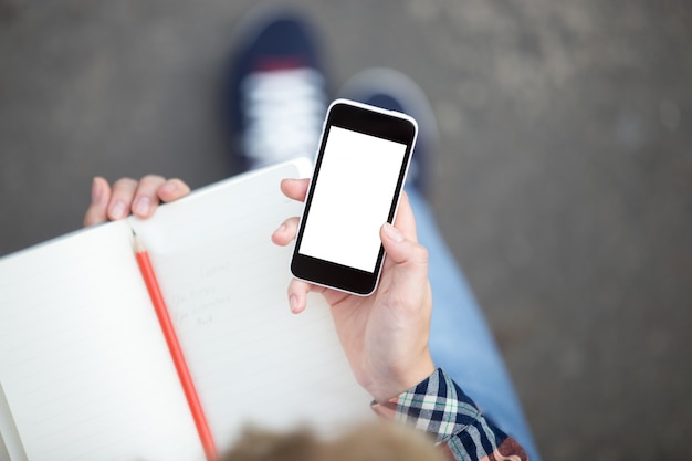 Mão segurando um smartphone contra um caderno com um lápis