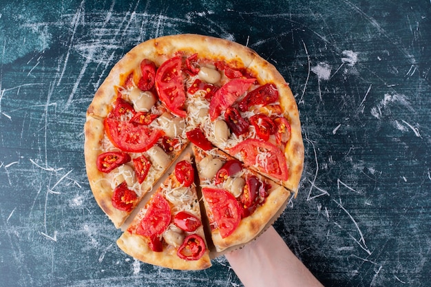 Mão segurando uma deliciosa pizza de frango com tomate em mármore.