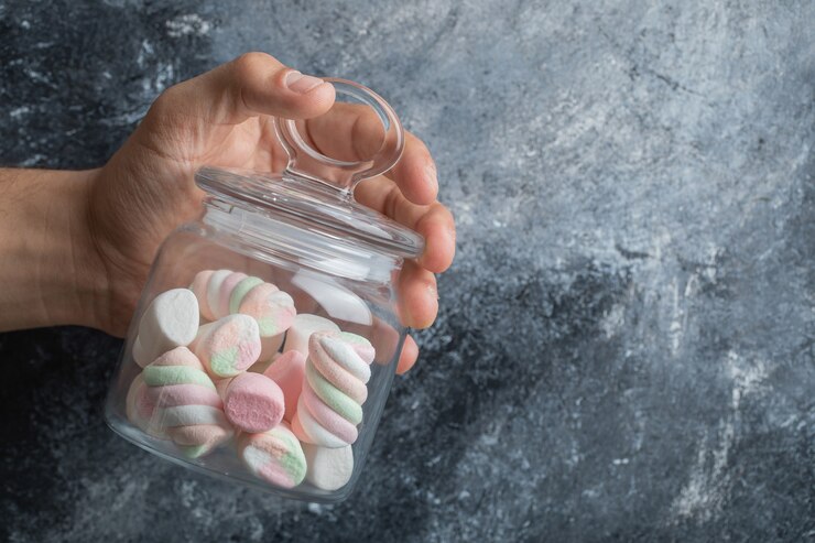 Foto grátis mão segurando uma jarra de vidro com deliciosos marshmallows em um fundo cinza.