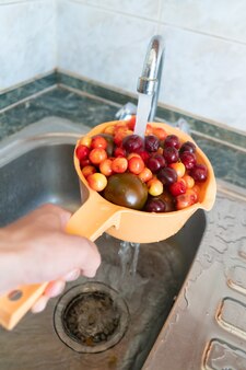 Mão segurando uma peneira com frutas frescas e bagas e lavando-a na cozinha com água