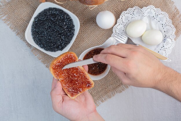 Mão slathers geléia no pão com faca.