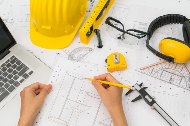 Mão sobre Construção planos com capacete amarelo e ferramenta de desenho