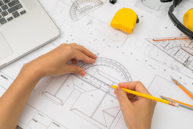 Mão sobre Construção planos com capacete amarelo e ferramenta de desenho
