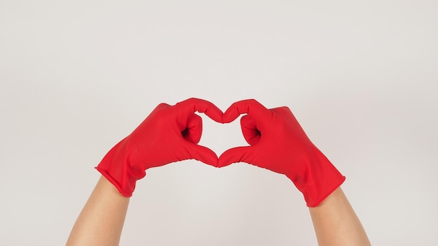 Mão usando luvas de látex vermelhas e sinal de mão de coração em fundo branco.
