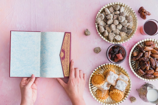 Mãos com alcorão na mesa com doces