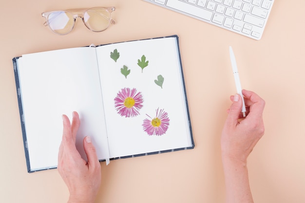 Mãos, com, caneta, perto, caderno, com, flores secas, teclado, e, óculos