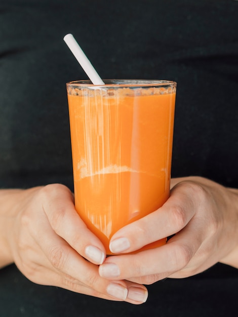 Mãos com copo de suco de cenoura