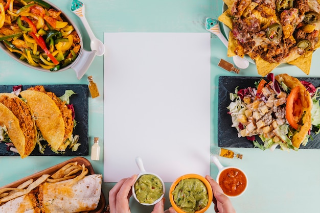 Mãos com guacamole perto de papel e comida