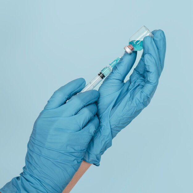 Mãos com luvas segurando vacina e seringa