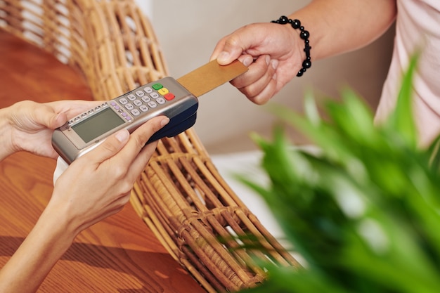Mãos da recepcionista do hotel segurando o terminal de pagamento quando o hóspede do hotel passa o cartão de crédito