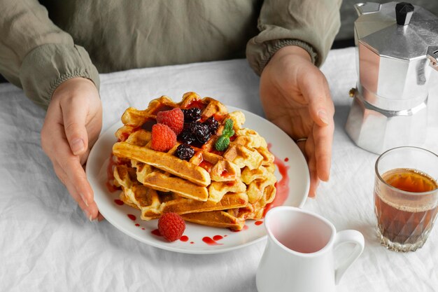 Mãos de alto ângulo segurando um prato com waffles