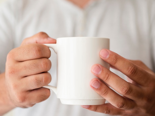 Mãos de close-up, segurando uma maquete de caneca