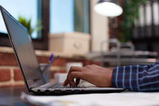 Mãos de empresário compondo e-mail no teclado do laptop sentado na mesa no escritório moderno da agência de marketing. Visão detalhada dos dedos de freelancer trabalhando em estatísticas de vendas no computador portátil.