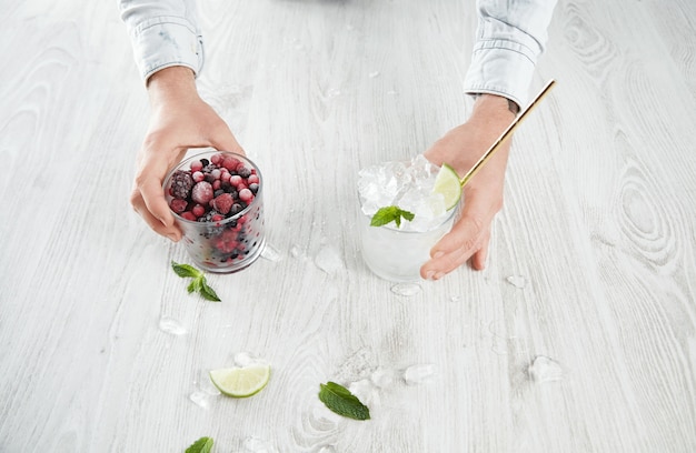 Mãos de homem com vista superior segurando copos com frutas congeladas e cubos de gelo com limão