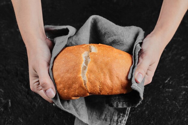 Mãos de homem cortando pão ao meio na mesa escura com toalha de mesa.