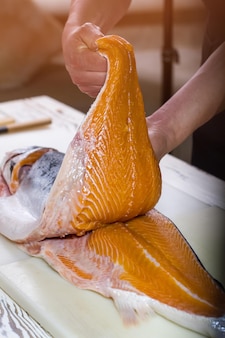 Mãos de homem segurando peixe cru. carne vermelha de peixe. salmão suculento para risoto. ingrediente essencial da cozinha japonesa.