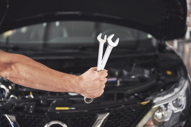 Mãos de mecânico de automóveis com uma chave inglesa na garagem.