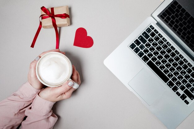 Mãos de mulher com caixa de presente de café e laptop com coração em fundo branco Dia dos namorados conceito de compras on-line fundo de férias Vista superior