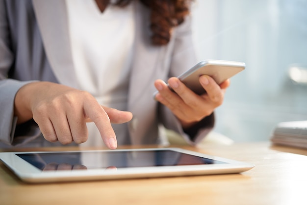 Mãos de mulher de negócios anônima usando tablet digital e smartphone no trabalho