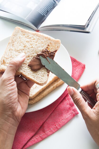 Mãos de mulher fazendo chocolate espalhar no fundo branco, prato branco, tiro claro