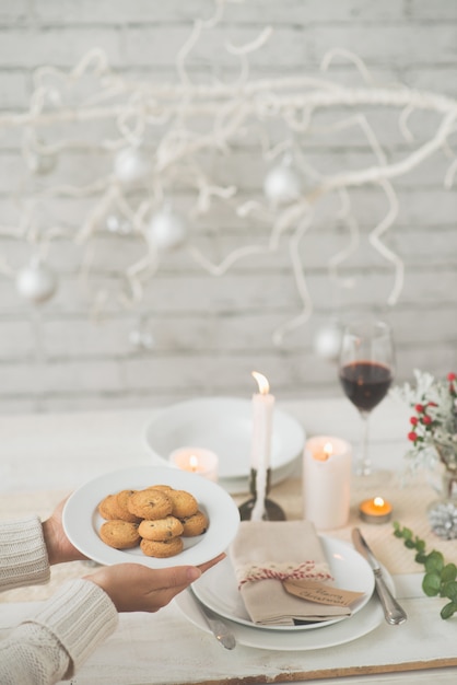 Mãos de mulher irreconhecível, carregando o prato de biscoitos para a mesa de jantar de natal