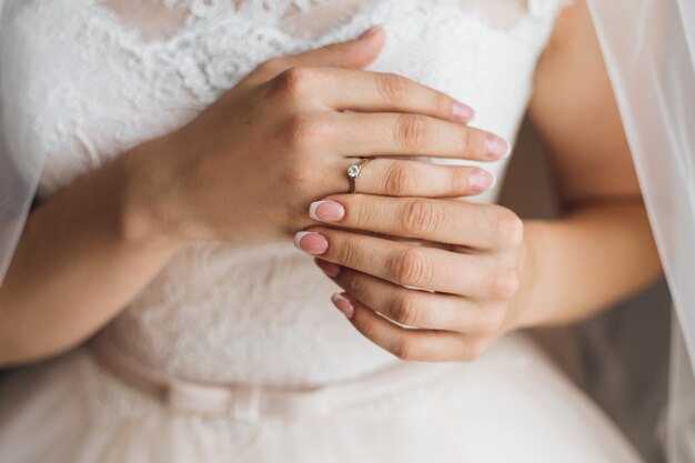 Mãos de uma noiva com concurso francês manicure e precioso anel de noivado com diamante brilhante, vestido de noiva