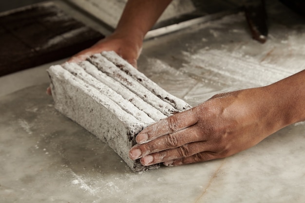 Mãos do chef negro segura barras de chocolate recém-assadas em açúcar em pó antes de embalar, closeup em confeitaria artesanal profissional