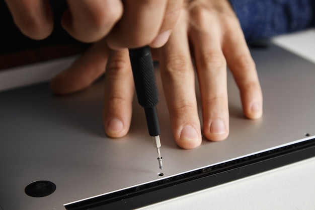 mãos do mestre desmontando uma pequena equipe com uma chave de fenda magnética, desmontando e consertando um laptop quebrado