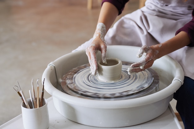 Mãos do oleiro feminino irreconhecível, fazendo o vaso de barro na roda de oleiro