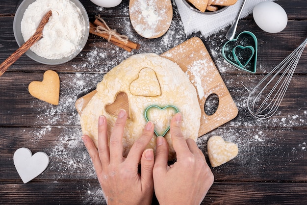 Mãos fazendo biscoitos em forma de coração dia dos namorados com utensílios de cozinha