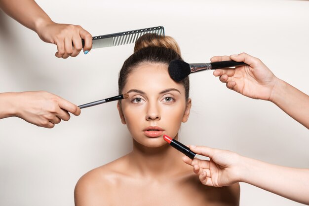 Mãos fazendo maquiagem e penteado de mulher jovem e bonita