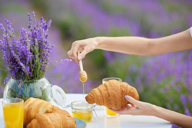 Mãos femininas colocando mel em croissants em um campo de lavanda