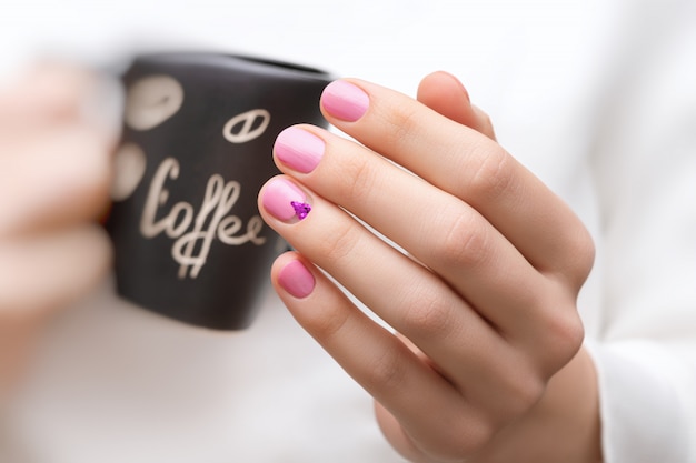 Mãos femininas com design de unha rosa segurando xícara preta.