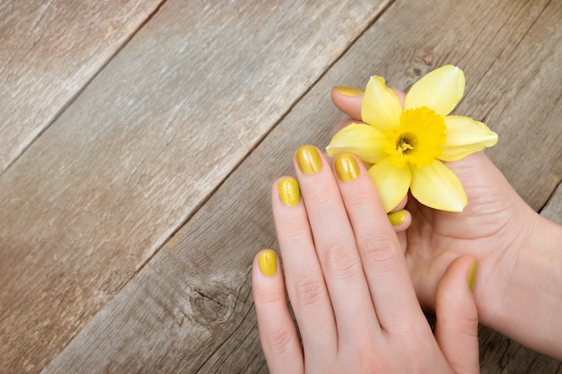 Foto grátis mãos femininas com manicure glitter amarelo segurando flor de narciso.