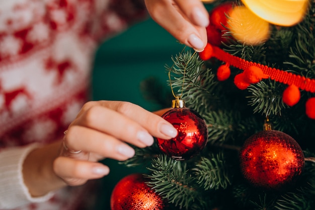 Mãos femininas fechem, decorando a árvore de Natal com bolas vermelhas